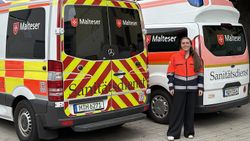 Eine junge Frau in Malteser Dienstkleidung steht zwischen zwei Einsatzfahrzeugen.