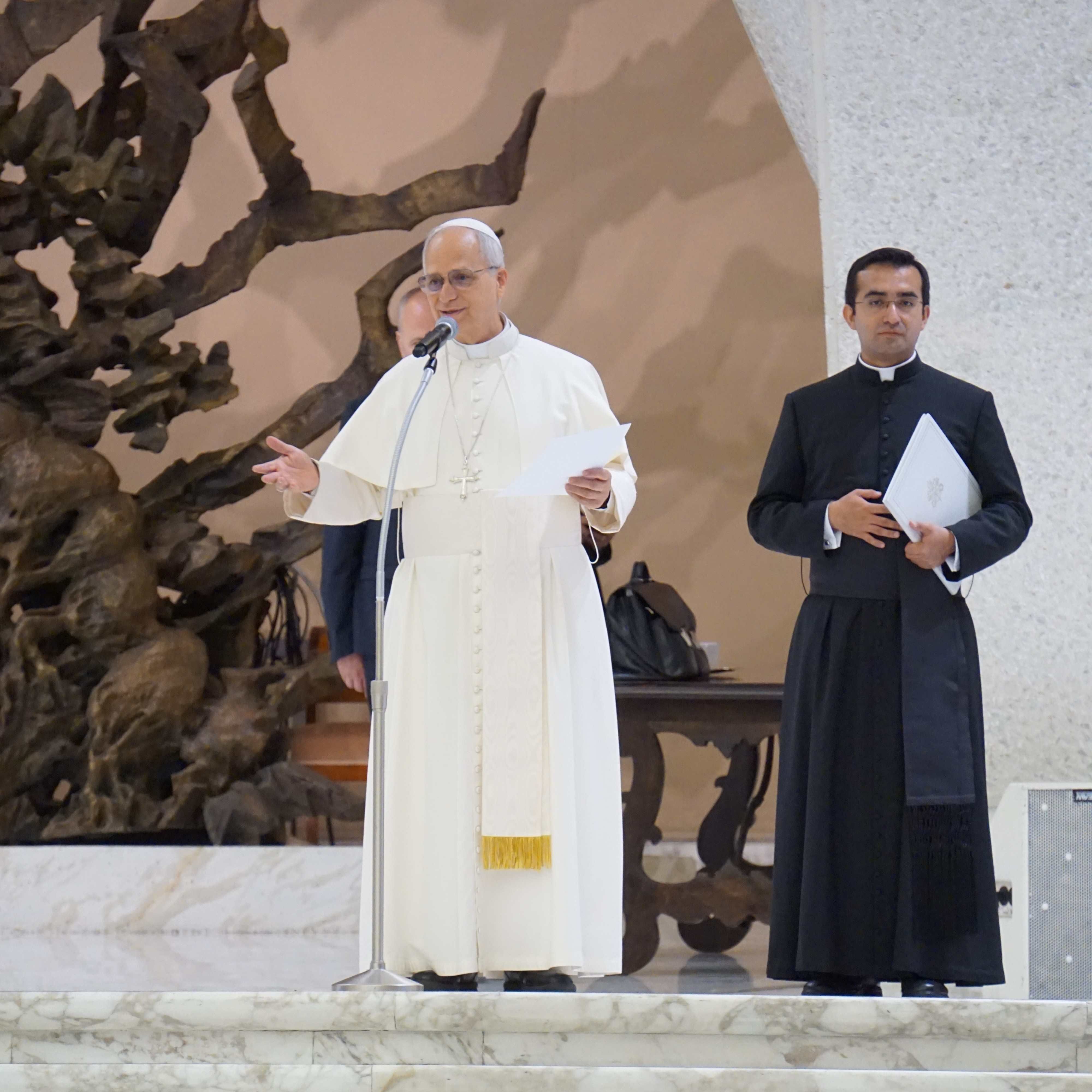Zwei Männer in liturgischer Kleidung, einer davon ist Papst Leo XIV. stehen vor einer großen, abstrakten Skulptur an einer Wand.