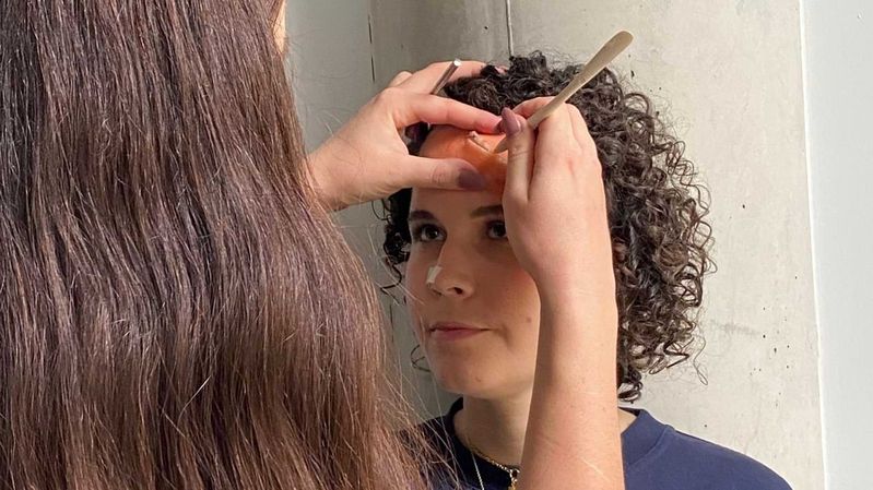 Eine Frau, die einer anderen Frau eine künstliche Wunde auf die Stirn modelliert. 