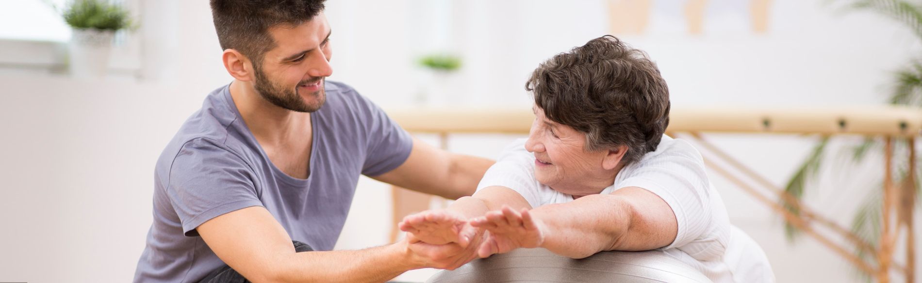 Physiotherapeut unterstützt ältere Patientin bei Dehnübung der Arme.