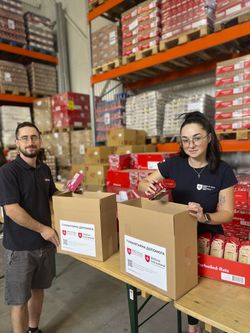 Eine Helferin und ein Helfer der Malteser packen Lebensmittelpakete für bedürftige Menschen in der Ukraine.