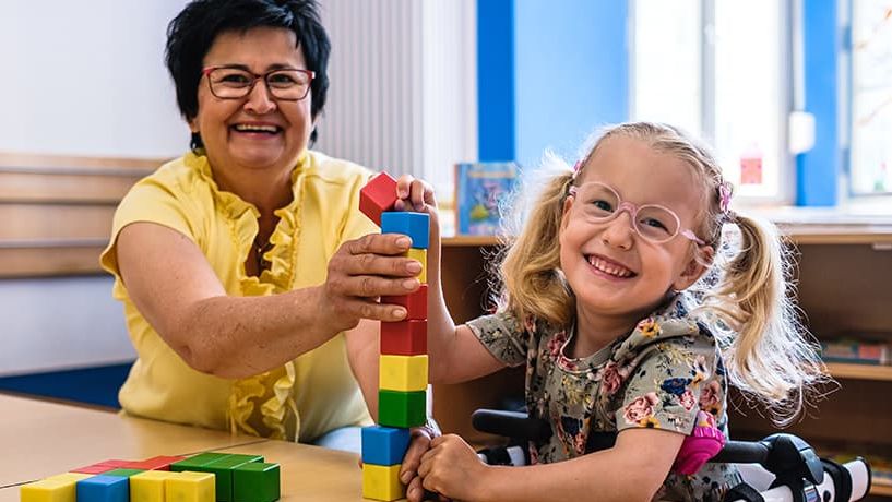 Eine Kita-Begleiterin baut mit einem Kind mit Bauklötzen. 