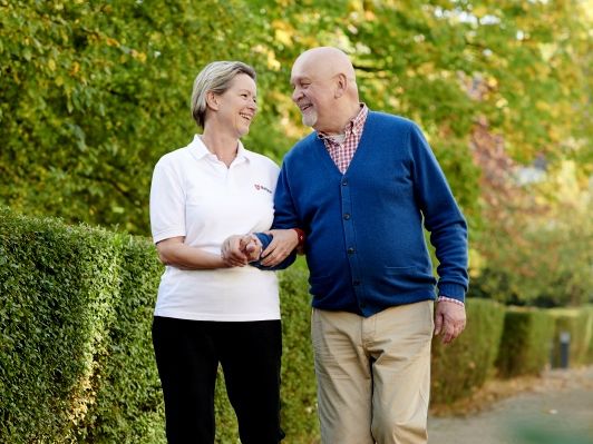 Eine ehrenamtliche Malteser-Helferin begleitet einen älteren Herrn auf einem Spaziergang