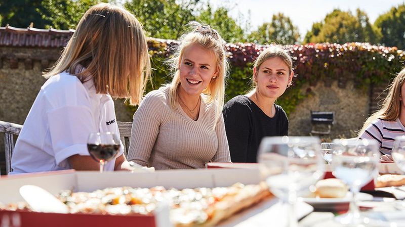 Junge Menschen an einem Tisch, auf dem Pizza und Getränke stehen 