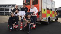 Sechs Jugendliche posieren in Malteser Kleidung und mit einem "abgerissenen Fuß" vor einem Rettungswagenu