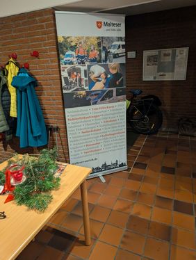 Das Roll-Up der Malteser Aurich listet die vor Ort angebotenene Dienste auf, ERste-Hilfe-Ausbildung, Hausnotruf, Fahrdienst, Sanitätsdienste, Mobiler Einkaufswagen, Auslandsdienst und Kulturbegleitdienst