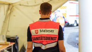 Malteser Sanitäter im Zelt von hinten fotografiert.