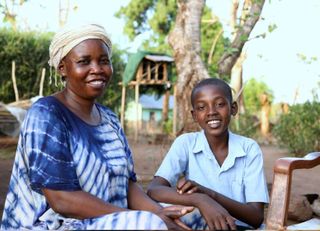 In einem Schulgarten im Südsudan sitzen eine Frau und ein Junge und lächeln in die Kamera