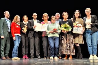 Zehn Personen stehen auf einer Bühne, zwei davon halten eine Urkunde.