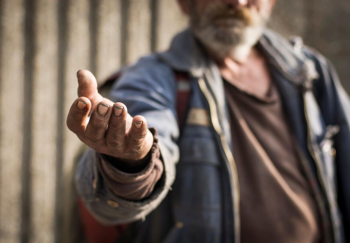 Obdachloser Mann streckt Hand aus.