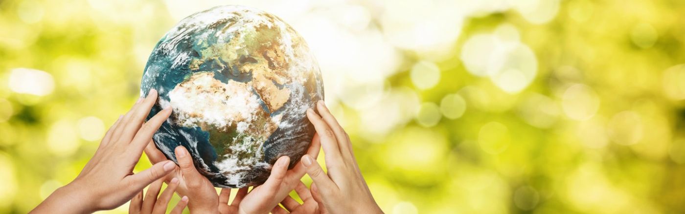 Hände von Kindern halten eine Weltkugel vor einem verschwommenen Blätterdach.