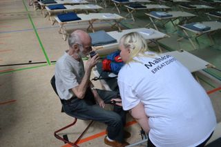Eine Malteserin spricht mit einem Mann in einer Turnhalle voller Feldbetten