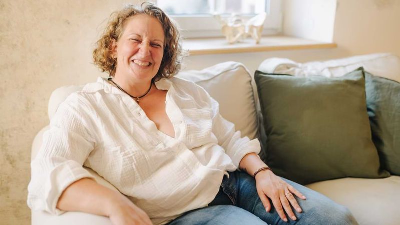 Eine lächelnde Frau in einem weißen Hemd auf einem Sofa. 
