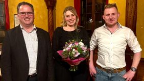 Eine Frau mit einem Blumenstrauß in der Hand steht zwischen zwei Männern.