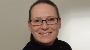 Nahaufnahme einer Person mit Brille vor neutralem Hintergrund.