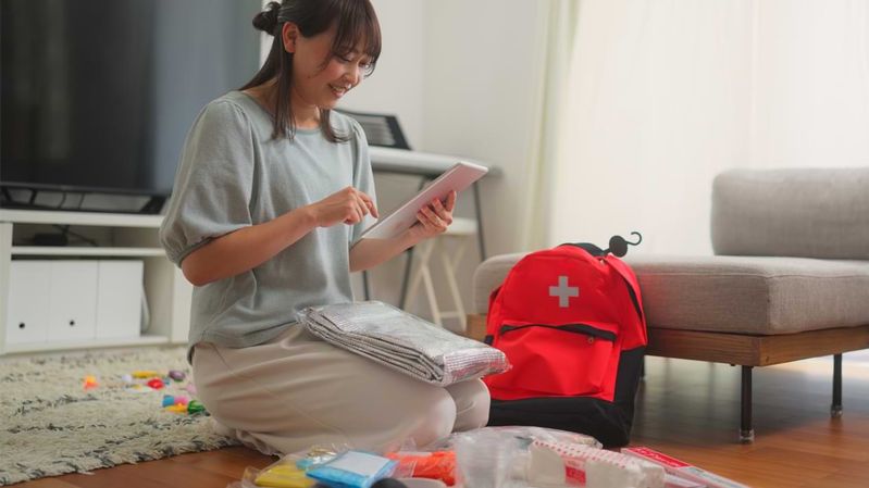 Eine junge Frau packt einen Rucksack mit Notgepäck auf dem Wohnzimmerboden.