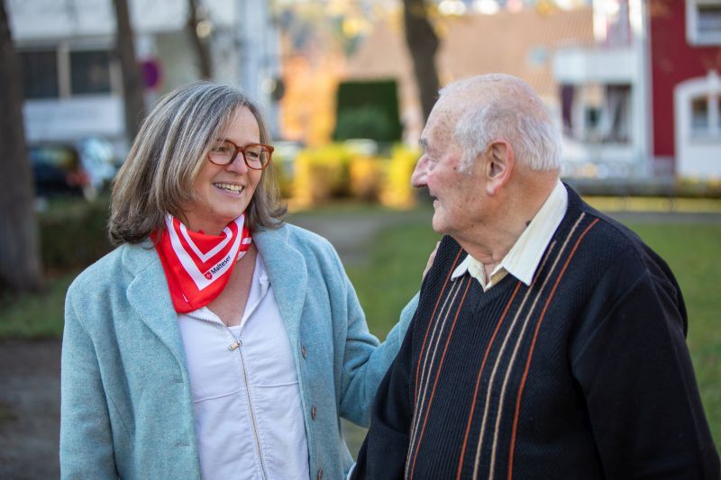 Frau mit einem Malteser Halstuch wendet sich einem älteren Herren im Pullover zu. 