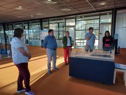 Fünf Personen stehen in einer modernen Ausstellungshalle um ein Architekturmodell in einer Vitrine.