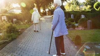 Zwei ältere Frauen trauern auf einem Friedhof.