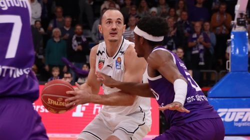 Spieler der Bamberg Baskets im weißen Trikot im Zweikampf mit einem gegnerischen Spieler in Lila während eines Spiels.