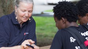 Ältere Frau zeigt jungen Flüchtlingen etwas auf dem Smartphone.