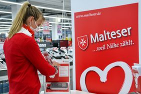 Eine Mitarbeiterin der Malteser steht am Stand des Hausnotruf im Media Markt und sortiert Flyer.