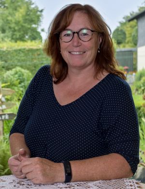 Lächelnde Frau mit Brille in einem Garten.