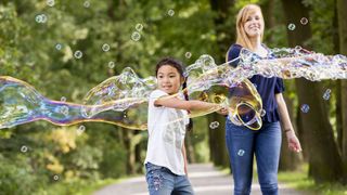 Junge macht große Seifenblasen und wird von Malteser Helferin begleitet.