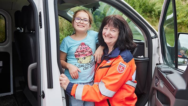 Mädchen im Fahrzeug der Malteser und Malteser Mitarbeiterin lachen.