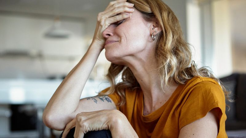 Eine Frau mit verzweifelten Gesichtszügen hält sich die Hand an die Stirn.