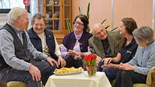 Senioren sitzen gemütlich im Café Malta mit einer Malteser Mitarbeiterin.