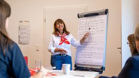 Eine Frau steht an einem Flipchart und erklärt etwas.