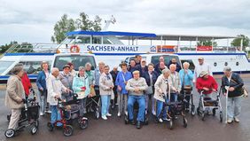 Mehrere ältere Männer und Frauen stehen vor einem Fahrgastschiff.