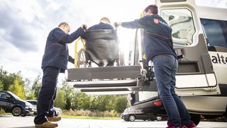 Zwei Mitarbeitende des Malteser Fahrdienstes helfen einer Person im Rollstuhl.