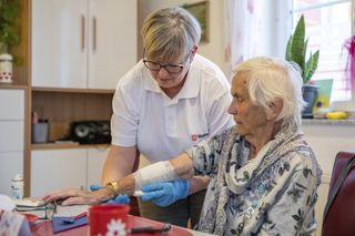 Mitarbeiterin im Pflegedienst legt einer älteren Dame zu Hause einen Verband an