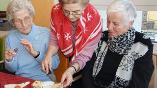 Malteser Helferin gibt zwei älteren Damen ein Stück Kuchen