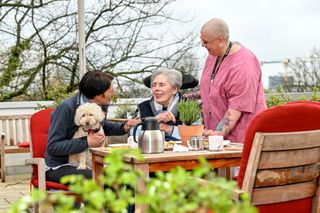 Drei Personen sitzen im Garten und trinken Kaffee