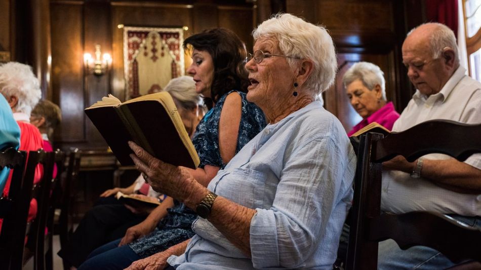 Alte Menschen mit Gesangsbüchern in Stuhlreihen. 