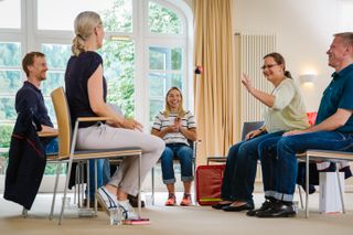 Menchen sitzen sich in Stühlen im Seminarraum gegenüber und sprechen und lachen miteinander