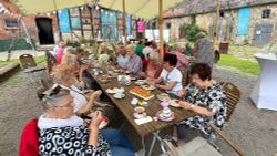 Viele Seniorinnen und Senioren sitzen an einem langen Tisch. Der Tisch ist mit Kaffee und Kuchen gedeckt.
