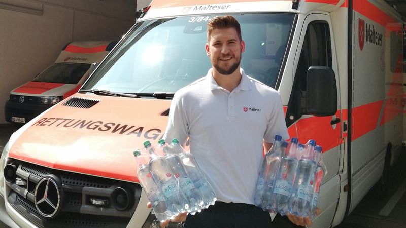 Junger Mann mit Wasserflaschen vor Rettungswagen