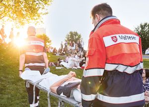 Malteser Einsatzsanitäter tragen einen Verletzten über ein Festivalgelände.