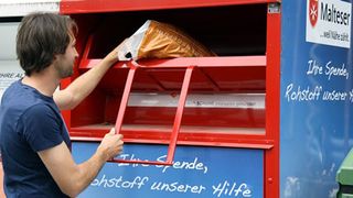 Mann wirft Altkleidung in einen Container der Malteser