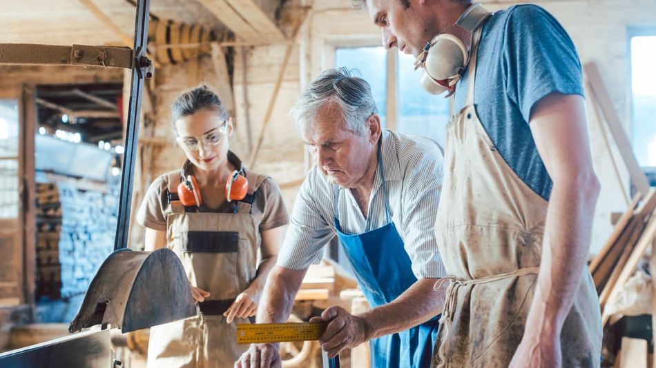 Ein alter Mann arbeitet mit einem jungen Mann und einer jungen Frau in einer Werkstatt.