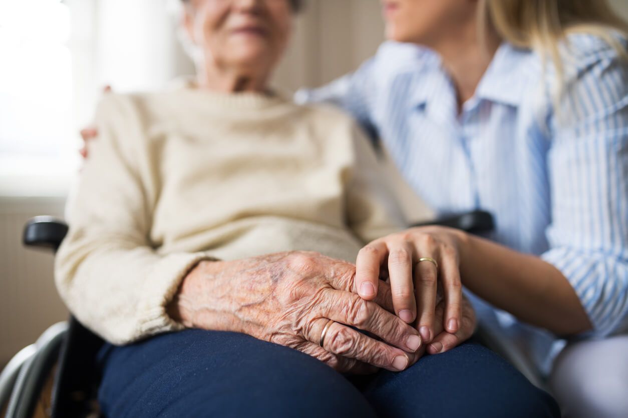 Eine ambulante Pflegekraft hält die Hand einer Seniorin im Rollstuhl.