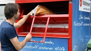 Mann wirft Altkleidung in einen Container der Malteser