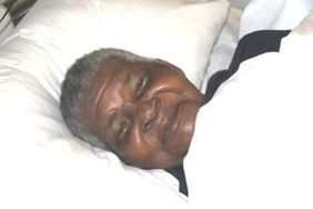 Grace Mbonambi smiles while resting on a white pillow.