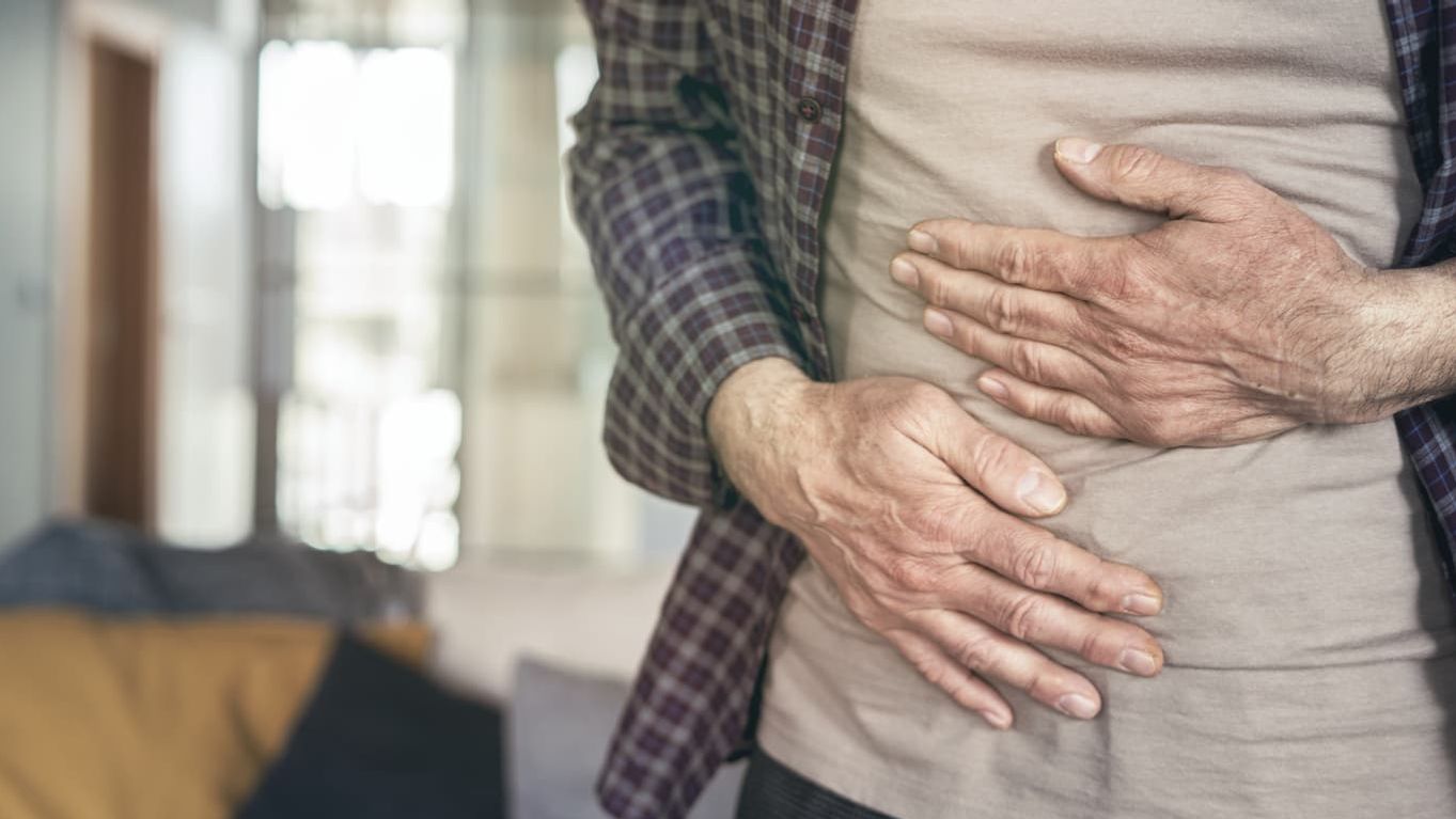 Hände umklammern den Bauch, sodass diejenige Person Schmerzen am Bauch hat.