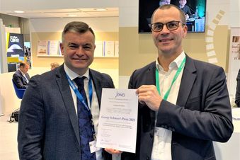 Zwei Männer im Anzug halten gemeinsam eine Urkunde mit der Aufschrift „Georg-Schwedt-Preis 2023“ in die Kamera.