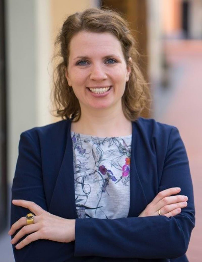 Porträt einer lächelnden Frau mit verschränkten Armen.